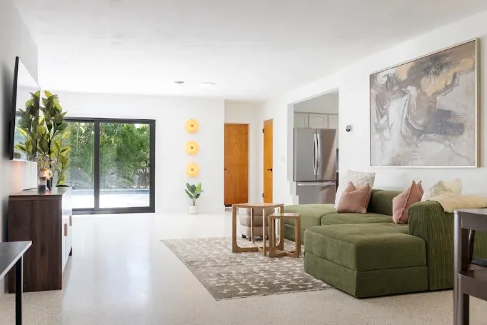 An open living room with a green sectional, sliding doors to a pool deck, and a large abstract canvas