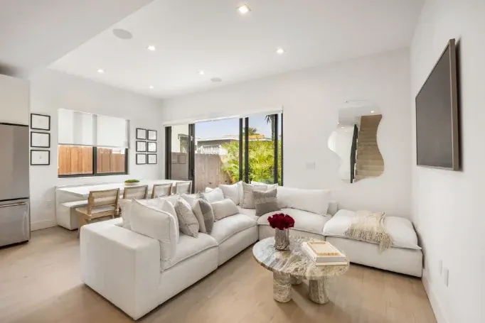 A white living room with a curved sectional, a marble coffee table, and sliding doors to the garden